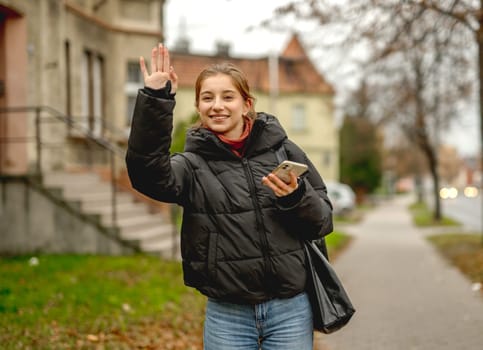 Happy Girl Waving To Someone On A Blurred Street Background