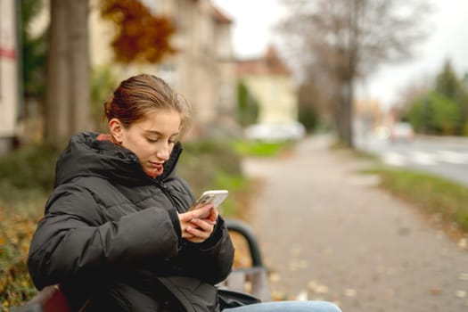 Sweet Girl Scrolling Phone While Sitting On Bench Outside
