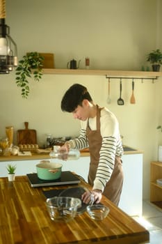 Happy Asian man cooking at home with fresh ingredients.