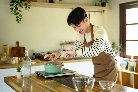 Happy Asian man cooking at home with fresh ingredients.
