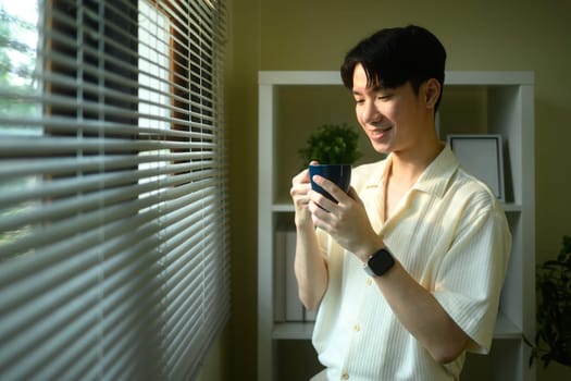 Relaxed man enjoying coffee by the window at home.