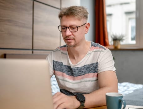 Man Working Remotely On Laptop At Home In Bedroom