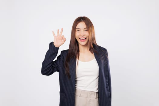 OK sign ok approval by a happy Asian woman smiling and gesturing success with her fingers isolated on a clean white background showing confidence and business agreement