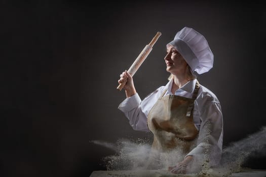 An elderly cook playfully poses with a rolling pin, surrounded by flour, capturing a lighthearted moment in her kitchen.