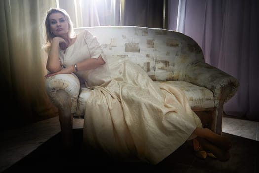 A middle-aged blonde blogger relaxes elegantly on a sofa during an indoor lifestyle photo shoot at home.