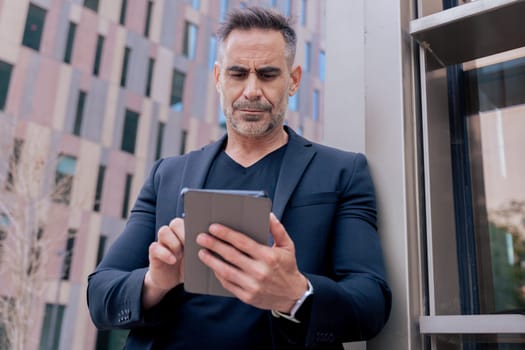 Confident businessman standing outdoors using a tablet in a modern urban setting. He appears focused and professional. Concept of digital work, technology, and contemporary business lifestyle.