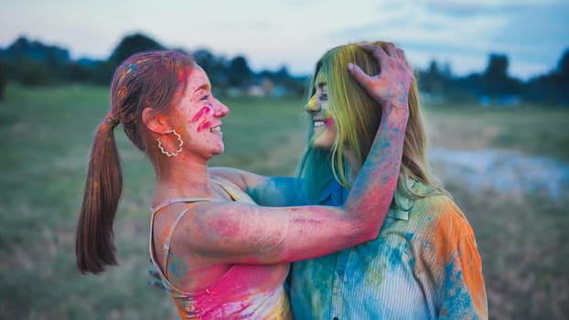 Two school friends, both females, embrace while covered in vibrant powder paint, celebrating the holi festival in a field at sunset