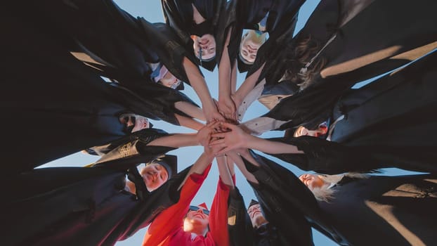 Graduates wearing academic gowns join hands in a circle, symbolizing unity, achievement, and the start of a new chapter in their lives