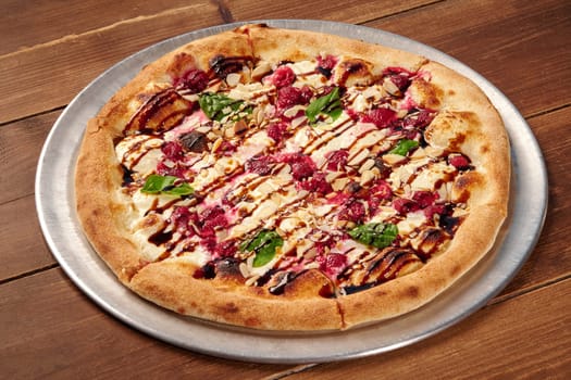 Gourmet pizza features fresh raspberries, toasted almonds, balsamic glaze, basil, and creamy white sauce, creating a sweet and savory culinary experience