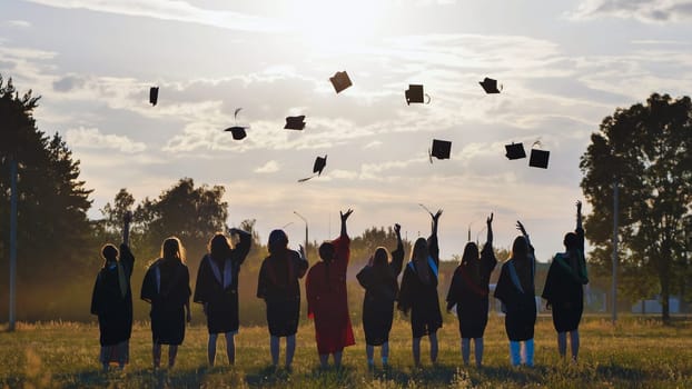 Group of students joyfully celebrating graduation, tossing their caps high into the air against a stunning sunset backdrop