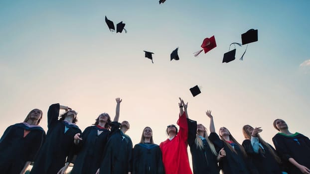 Group of cheerful graduates celebrating their graduation by tossing their caps into the air against a beautiful sunset sky