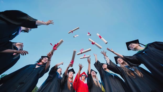 Students happily tossing diplomas in the air in celebration of their academic success, while dressed in graduation attire with a beautiful blue sky in the background