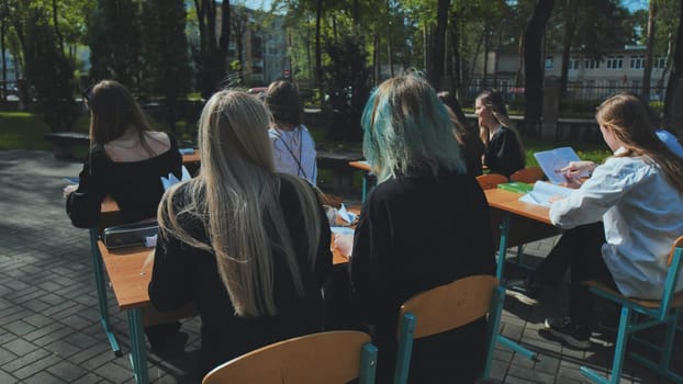 Group of high school students sitting at desks outdoors, learning and studying together on a bright sunny day
