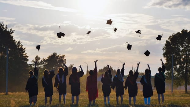 Group of students joyfully celebrating graduation by tossing their caps into the air against a stunning sunset backdrop