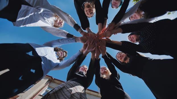 Group of happy students joining hands forming a circle, celebrating school day, viewed from below against a blue sky