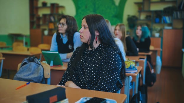 Teenage students are attentively listening to their teacher in a classroom during a school day, focusing on the lesson