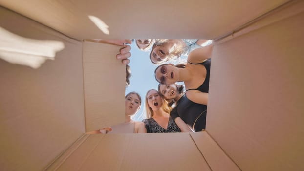 Group of surprised high school students opening a cardboard box against a blue sky during summer