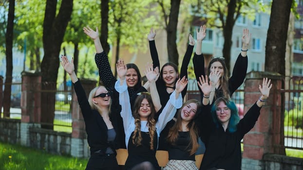 Group of cheerful students raising their hands outdoors, celebrating the end of school day