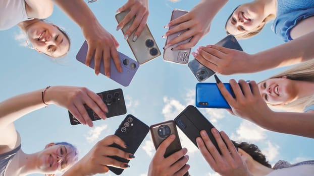 Group of happy students holding smartphones, making a circle with their devices, and enjoying their time together