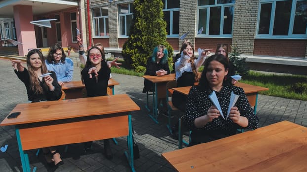 Cheerful students enjoying a sunny day in the schoolyard, playing with paper airplanes and sharing laughter after class