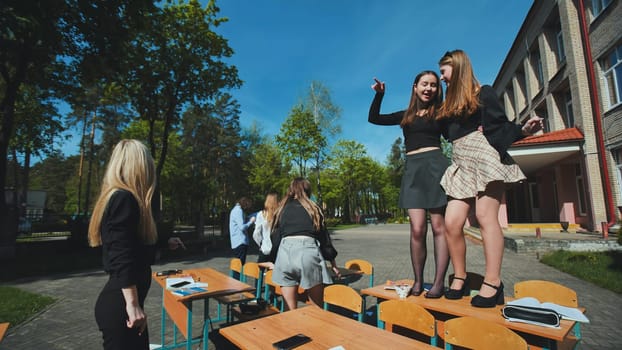 Group of teenage girls dancing on school desks in the schoolyard after their classes, enjoying their free time and celebrating the end of the school day
