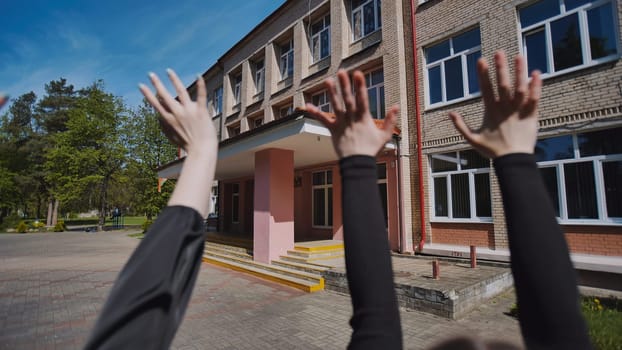 Students raising their hands in front of the school building on a sunny day to celebrate the end of the school year