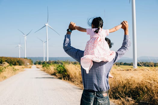 Dad carries daughter at wind farm exploring future. Family bonding near turbines signifies innovation in renewable energy. A joyful father-daughter moment in the windmill industry. father day concept