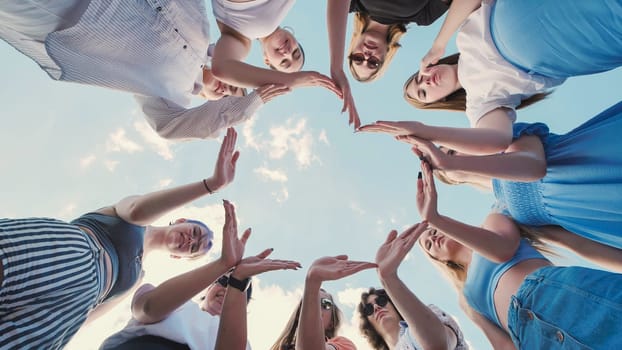 Group of school friends forming a circle with their hands, symbolizing unity, teamwork, and friendship against a cloudy sky
