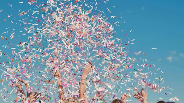 Group of cheerful high school students throwing colorful confetti in the air celebrating graduation under a bright blue sky