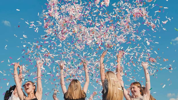 Group of high school students throwing colorful confetti in the air celebrating graduation under a bright blue summer sky