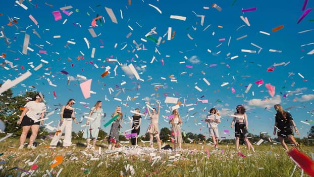 Group of friends joyfully celebrating graduation while throwing colorful confetti in a vibrant field under a bright blue sky