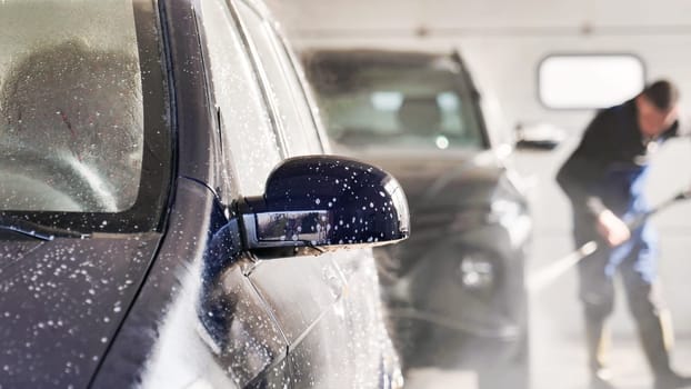 Car wash worker cleaning vehicle with high pressure water jet in a car wash service