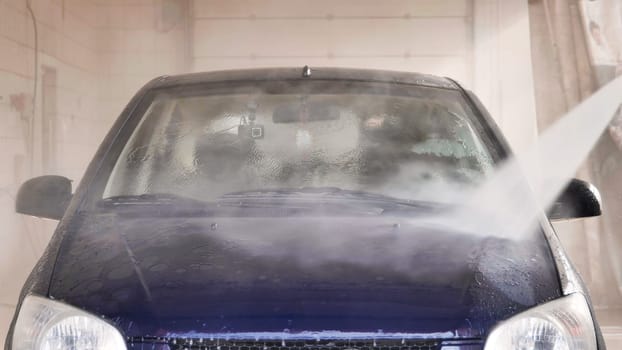 Car wash worker cleaning windshield with high pressure water jet during a car wash