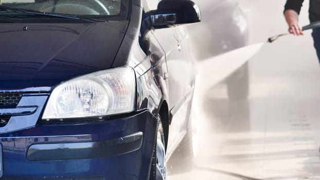 Car wash worker is using a high pressure water jet to clean a vehicle