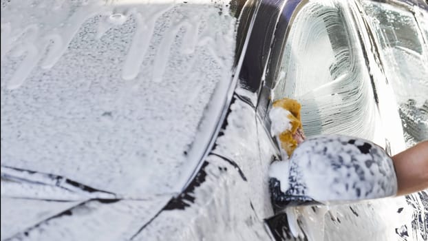 Car wash worker is cleaning a vehicle with a sponge and soap