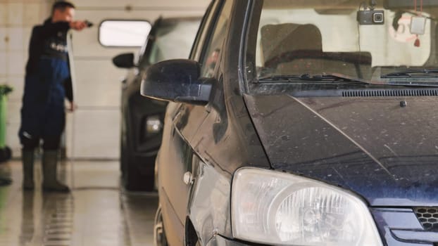 Car wash worker cleaning vehicles with high pressure water jet in a garage