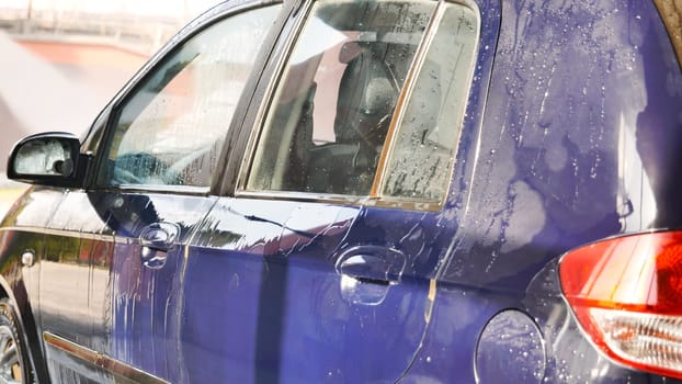 Professional car wash worker cleaning a purple car using a high pressure water jet