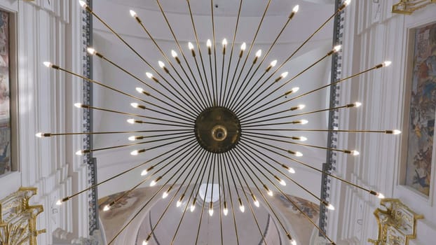 Low angle view of a starburst chandelier hanging from a church ceiling, illuminating the space and showcasing the frescoed walls