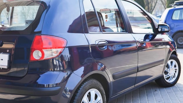 Freshly washed dark blue car gleaming under sunlight, parked on paved city street