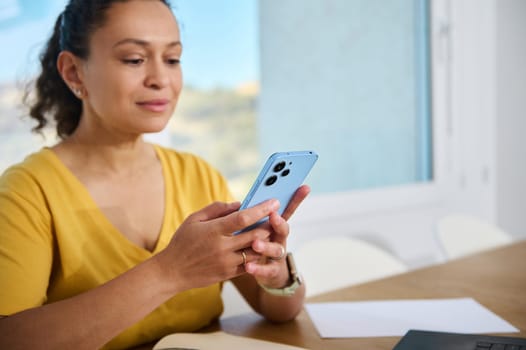 A woman in a brightly lit home office uses her smartphone. The serene setting conveys casualness and focus, emphasizing the ease of technology in everyday life and remote work setups.