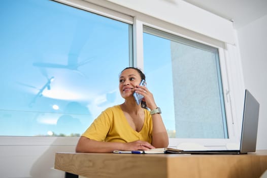 Person working in a minimalist home office, conversing on the phone while seated with a laptop, embodying relaxation, productivity, and remote work.