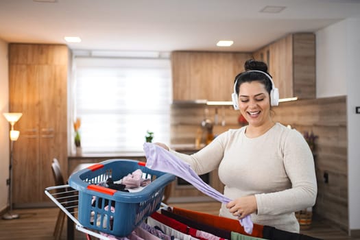 Woman listening to music while hanging the laundry on drying rack at home.