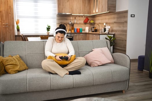Competitive woman with wireless headphones playing video game at home.