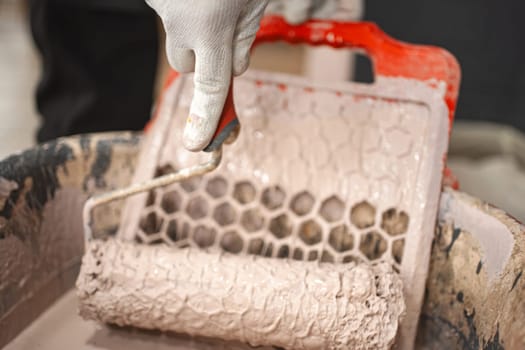 Close-up of a paint roller spinning on a strainer above a large red bowl.