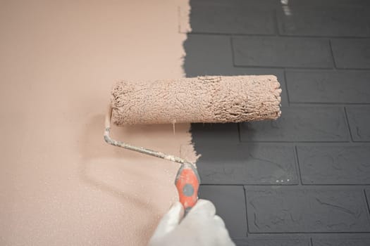 A person standing in front of a wall with a roller, applying paint in smooth, even strokes. The wall is being transformed from its original color to a new shade.