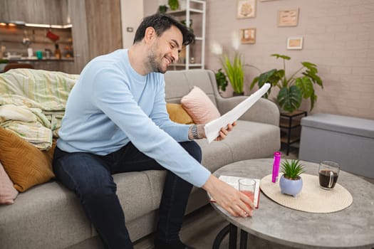 Smiling man is seated on a couch, engrossed in reading a bills. The room is well-lit, with the man focused on the pages of his bills.