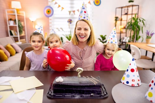 A woman and children share laughter at a festive birthday gathering.