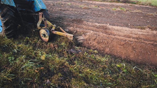 Old blue tractor plowing the field creating a single furrow, preparing the soil for sowing