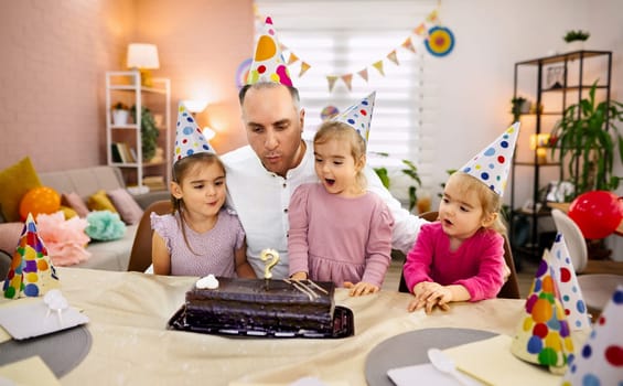 A father shares a joyful moment with his daughters on a birthday.