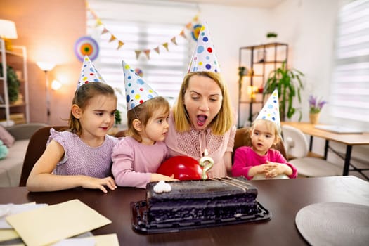 A woman and three young girls celebrate a birthday with cake and balloons.